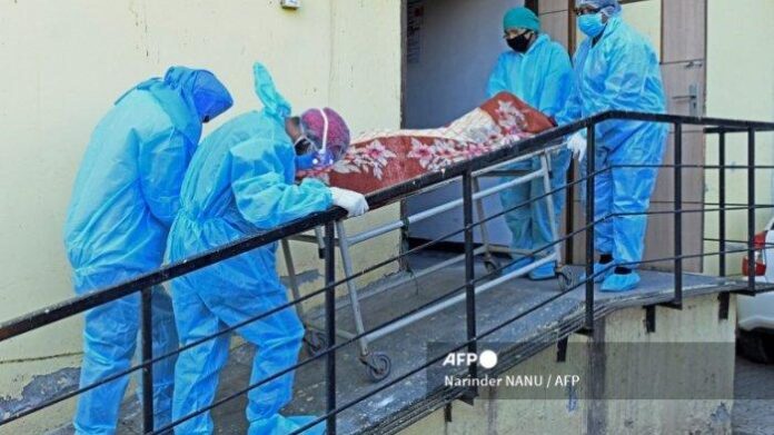 Anggota staf medis yang mengenakan APD membawa jenazah pasien Covid-19 di sebuah rumah sakit di Amritsar, India pada 24 April 2021.