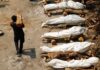 Seorang pria membawa kayu berjalan melewati tumpukan kayu pemakaman orang-orang yang meninggal karena Covid-19 saat kremasi massal, di sebuah krematorium di New Delhi, India, 26 April 2021. /Reuters/Adnan Abidi