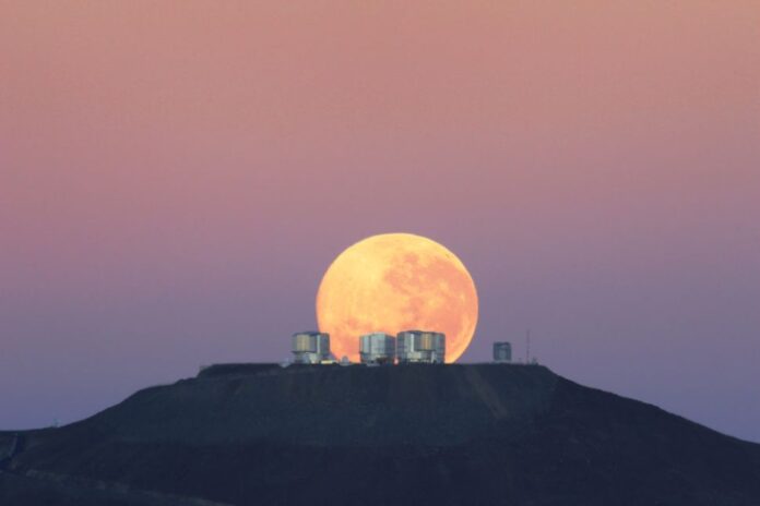 Bulan purnama tampak masif saat terbenam di belakang Teleskop Raksasa di Gurun Atacama Chili, dalam rilis foto ini pada 7 Juni 2010. Mengapa pengamat melaporkan bahwa bulan terlihat lebih besar di dekat cakrawala daripada tinggi di langit? Ini mungkin tidak lebih dari tipuan perspektif. (Foto: Gordon Gillet / ESO via Space.com)