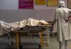 Seorang pria berdiri di samping tubuh istrinya, yang meninggal karena sesak napas, di dalam bangsal darurat rumah sakit yang dikelola pemerintah, di tengah pandemi penyakit coronavirus (COVID-19), di Bijnor, Uttar Pradesh, India, 11 Mei. , 2021. REUTERS / Denmark Siddiqui