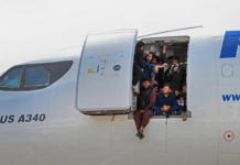 Orang-orang Afghanistan naik ke pesawat dan duduk di pintu pesawat tersebut saat rbuan orang memenuhi bandara Kabul untuk pergi dari negara yang sedang kacau-balau oleh Taliban. [Wakil Kohsar/AFP]