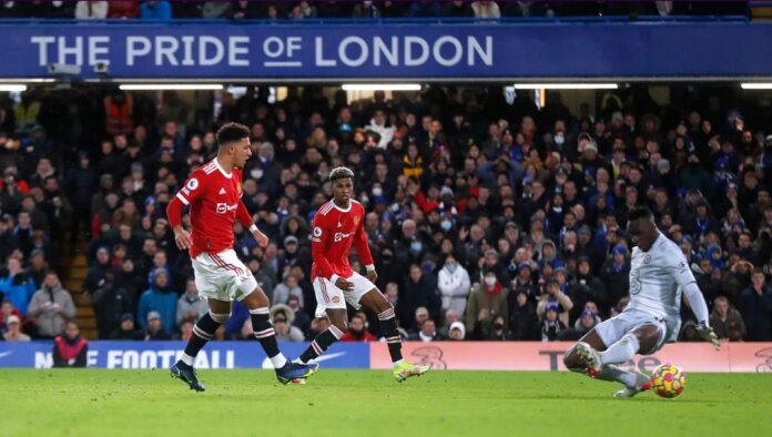 Jadon Sancho menembak melewati kiper Chelsea Edouard Mendy untuk mencetak gol keduanya bagi Manchester United sekaligus gol pertamanya di Liga Premier Inggris dalam hasil imbang 1-1 ves Chelsea di Stamford Bridge, Minggu (28/11/2021). (Foto dari Premierleague.com).