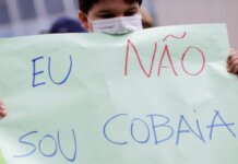 Seorang anak memegang poster bertuliskan 'Saya bukan kelinci percobaan' saat demonstrasi menentang paspor Covid dan vaksinasi wajib untuk anak-anak. (Foto: Ueslei Marcelino/Reuters via Guardian)