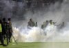 Polisi dan tentara berdiri di tengah asap gas air mata saat kerusuhan pada pertandingan sepak bola antara Arema Vs Persebaya di Stadion Kanjuruhan, Malang, Jawa Timur, 1 Oktober 2022. Ratusan orang dilaporkan meninggal dunia dalam tragedi kerusuhan tersebut. (AP Photo/Yudha Prabowo)
